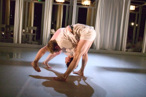 Two figures in white shirts with bare legs in movement in a duet