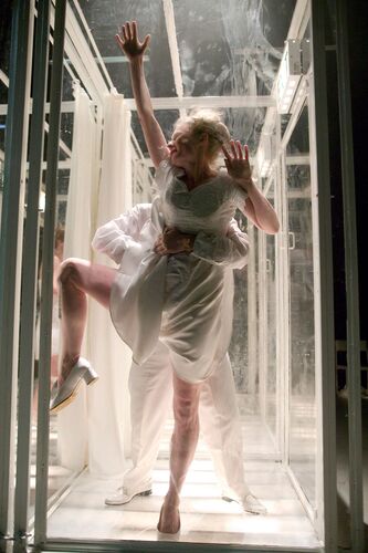 A figure pressed up against a smudged perspex wall in movement with another holding her from behind