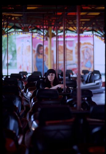 A lone figure sitting in a dodgem car among other empty cars on a dodgem track