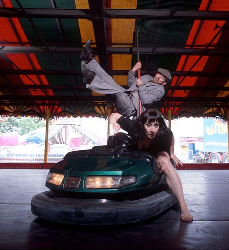 One figure in movement out of a dodgem car with another swinging from the dodgem car pole behind