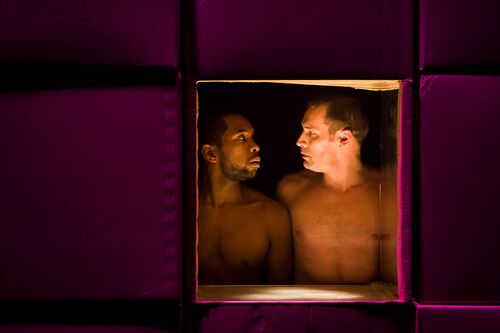 Two figures' bare torsos inside the framing of a box, looking at each other