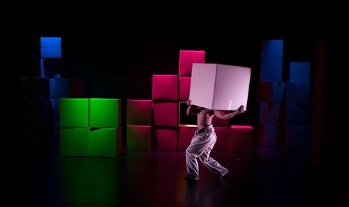 A topless figure with a large box held overhead in front of a backdrop of other boxes
