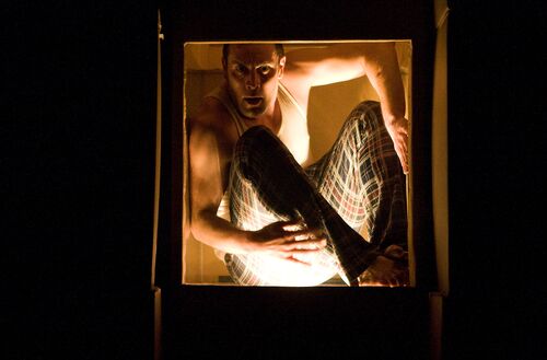 A figure curled up inside a box lit from within