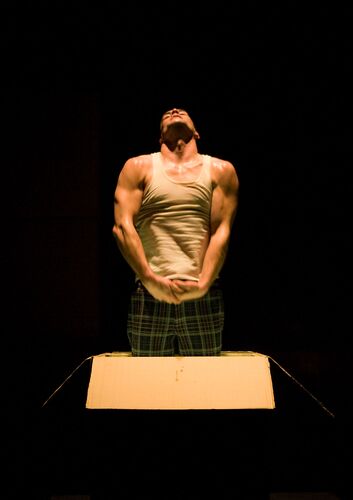 A figure spotlit on a black background in movement with his face raised to the ceiling