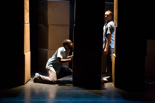 Two figures seen in side profile on either side of a stack of boxes