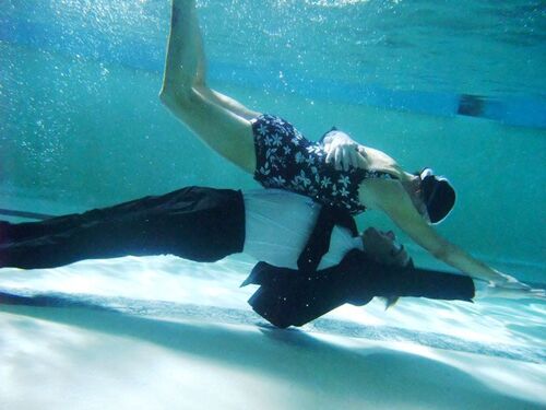 Two figures horizontal underwater - one in swimming togs and the other in a suit