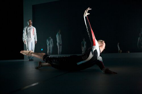 A figure in mvoement on the floor with another figure approaching in the background