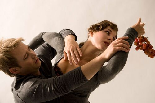 Two figures in movement with arms intertwined and one figure holding a bunch of grapes