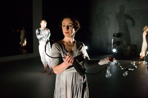 A figure standing holding a string of festoon lightbulbs trailing behind