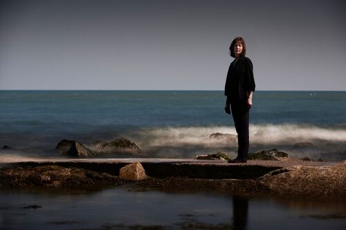 A figure standing looking to camera along a seascape