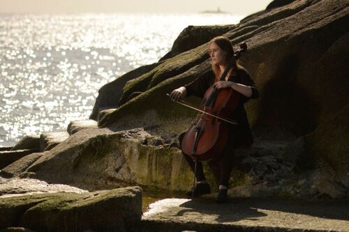 A cellist sitting playing by the sea