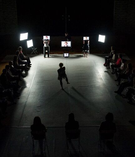 A figure silhouetted dancing on a dark stage facing three screens