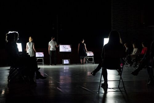 Three figures each standing beside a screen lit in the dark