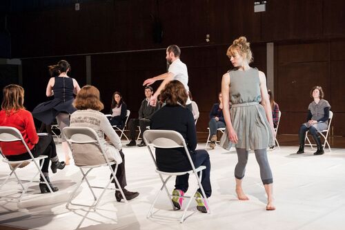 Justine Cooper walking around an audience member seated at the side of the performance space