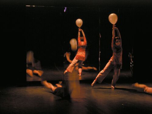 A figure in movement holding a balloon above her head with a mirror behind reflecting the stage