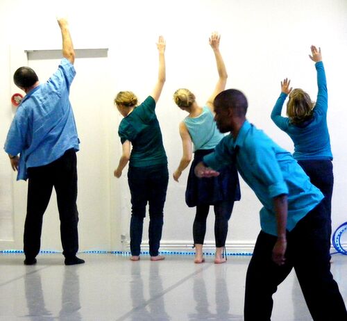 Four participants in movement along a wall in the background with someone in movement at the front