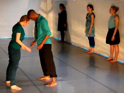 Two participants in movement with foreheads touching with others standing along the wall behind