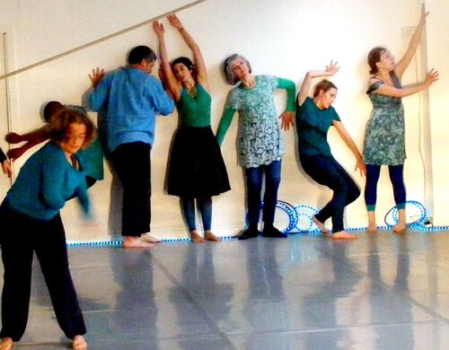 Participants in still poses along a wall with one figure in movement in space