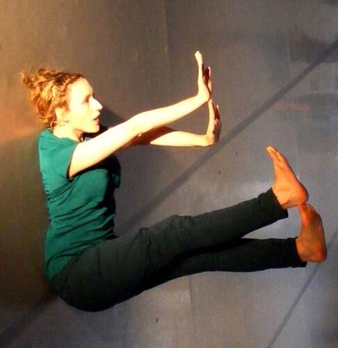 A participant in movement on the floor with arms and legs raised straight above them