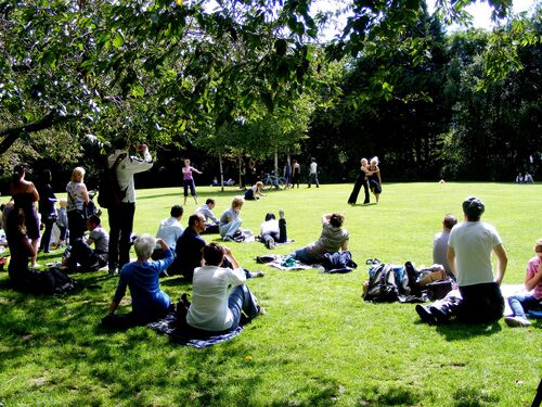 Two figures in movement performing for an audience seated on the grass