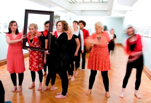 An ensemble of participants in movement with an empty picture frame in a gallery space