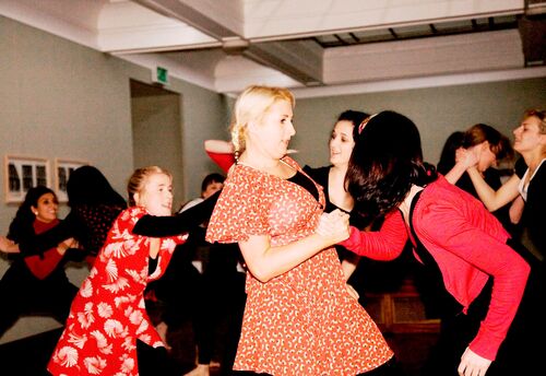 An ensemble of participants dancing in pairs in a gallery space