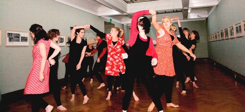 An ensemble of participants dancing in pairs in a gallery space
