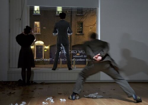 Three participants in movement seen from behind performing in front of a window to the street