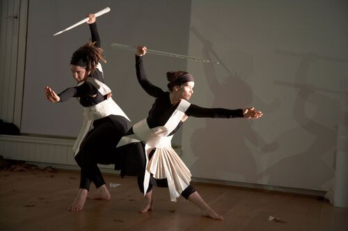 Two participants in movement each with long staffs in one hand