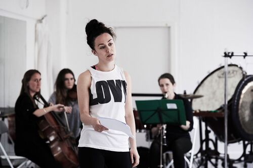 A figure standing with a script with three musicians playing in the background