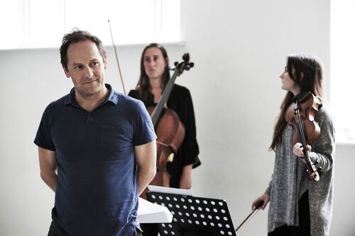 A figure standing with two musicians seen in the background