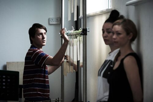 One figure adjusting a bar with two other figures leaning against the wall