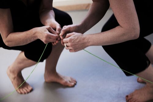 Two figures clutching green thread between their clasped hands