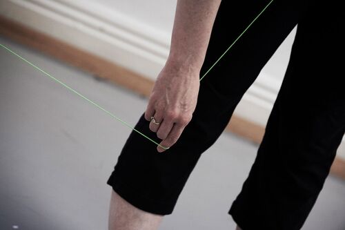 Green thread passing through a hand held down by a figure's leg