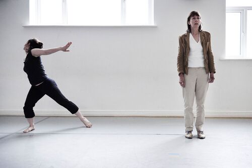 One figure standing on the right and another in movement on the left in a studio