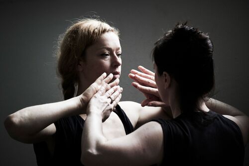 Two figures facing each other with palms touching by their faces