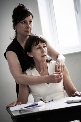 One figure seated with another standing behind with arms around her