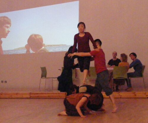 Five participants in movement with one walking over two others' backs