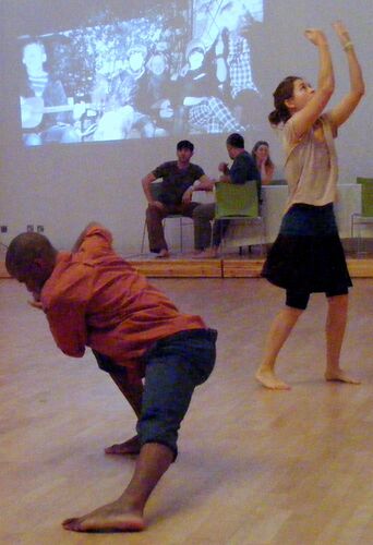 Two participants in movement with projections cast on a wall behind