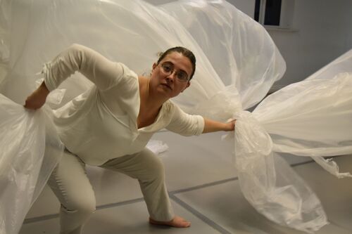 A participant in movement with large sheets of white plastic