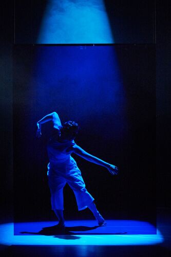 A figure lit in blue on stage in movement
