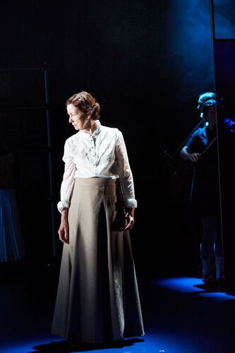 A figure standing on stage in a long skirt looking to the side