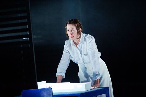 A figure standing dressed in white with hands braced on a blue table