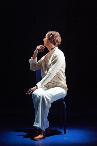 A seated figure dressed in white in side profile on stage