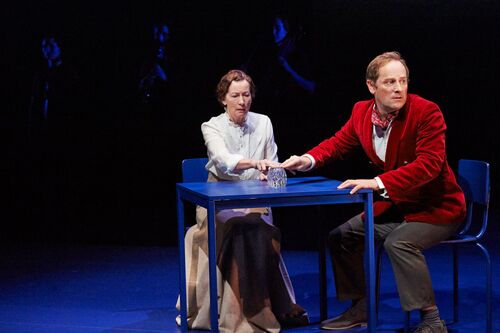 Two figures seated at a blue table on stage
