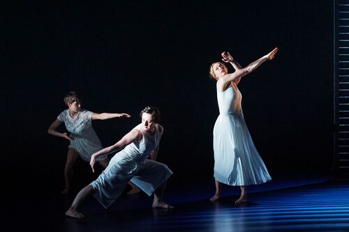 Three figures in movement dressed in white on a dark stage