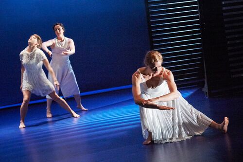 Three figures in movement dressed in white on a blue-lit stage