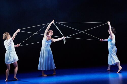 Three figures in white in movement with thread stretching between their hands