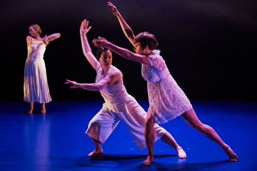 Two figures in a movement duet with another in movement in the background