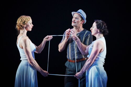 Two figures facing each other holding string in a square shape with a third figure standing between